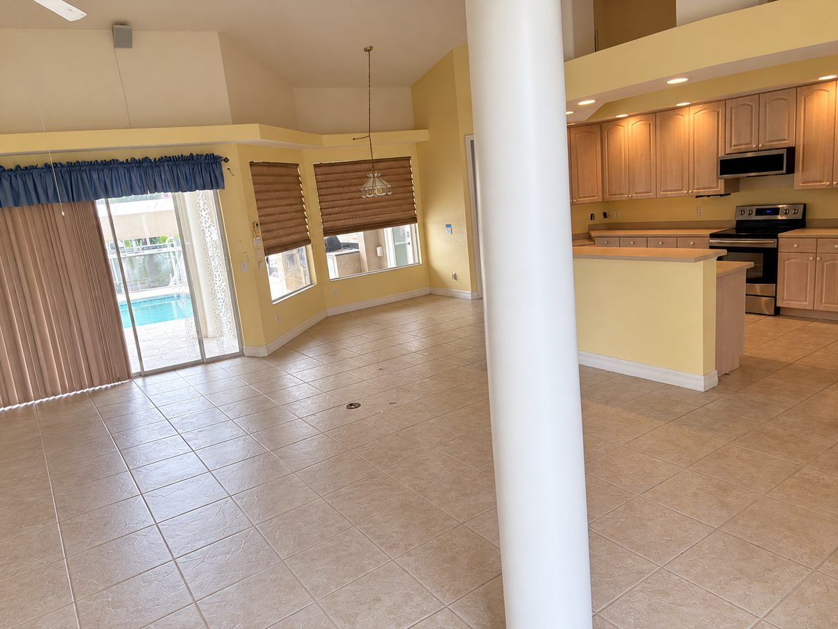 Completed cleanout: an empty open-plan living area and kitchen with bare tile floors, clear countertops and sliding glass doors to the pool.