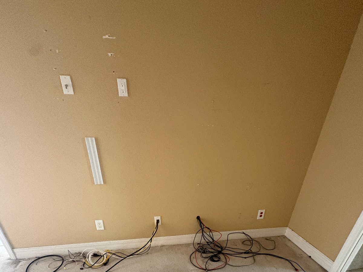 Completed cleanout: a carpeted room emptied to the walls, with loose cords left near the baseboard outlets.